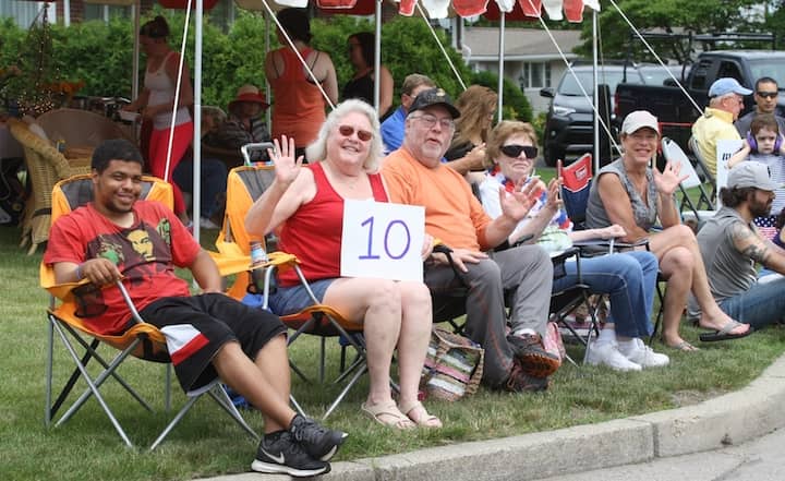 [CREDIT: Beth Hurd] Ginny Conway, 51, sits on the corner of Audubon and Narragansett Parkway with members of her family, holding up a "10" sign to cheer on her favorite groups as they march by.