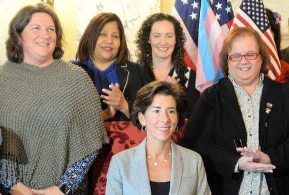 [CREDIT: Legislative Press and Information Bureau] Sen. Dawn Euer, left, and Rep. Camille F.J. Vella Wilkinson, right, applaud as Gov. Gina Raimondo, seated, signs legislation that extends veterans’ benefits to gay or transgender members of the armed forces denied honorable discharges due to sexual orientation at the State House today. With them are, from left, Sen. Ana B. Quezada and Sen. Bridget Valverde.