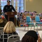 [CREDIT: RI State Police] WPD Col. Rick Rathbun speaks at Buttonwoods Community Center Dec. 17. Seated, from right, are Mayor Joseph Solomon, and U.S. Attorney Aaron L. Weisman. Standing at right is Colonel James M. Manni, Superintendent of the Rhode Island State Police.