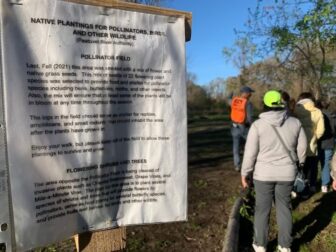 [CREDIT: Rob Borkowski] Pawtuxet River Authority volunteer Doug Wilson leads a tour through the Howard Conservation Area. Above, the group passes a sign explaining the role of polinators in aiding native plants.