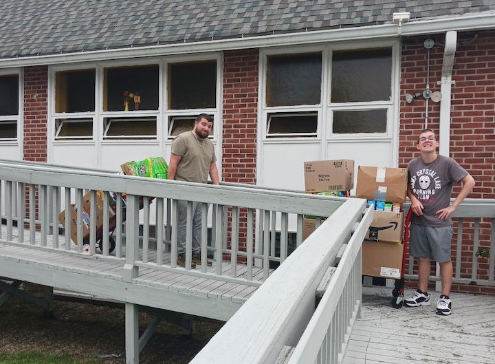 [CREDIT: Lincoln Smith, Photographic Society of RI] From left, Jordan Hiatt and Lucas Franco from WestBay Marketplace bringing cereal from the Lakewood Baptist Cereal Challenge out to load in the van for delivery to WestBay Marketplace.