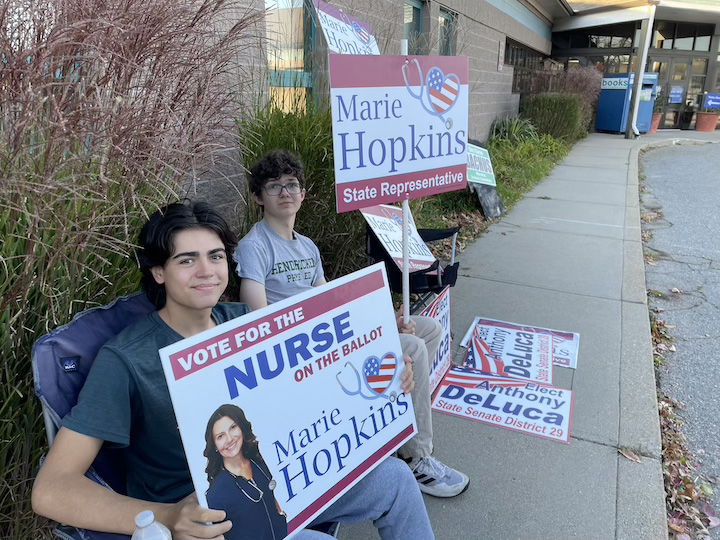 [CREDIT: Rob Borkowski] Jacob Scott and Alex Hopkins holding signs for Alex's mom, Republican Dist. 21 candidate Marie Hopkins, outside Pilgrim Senior Center Nov. 5, 2024.